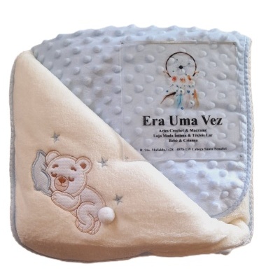 Cobertor infantil azul com relevo de bolinhas e lado creme com urso bordado e etiqueta transparente