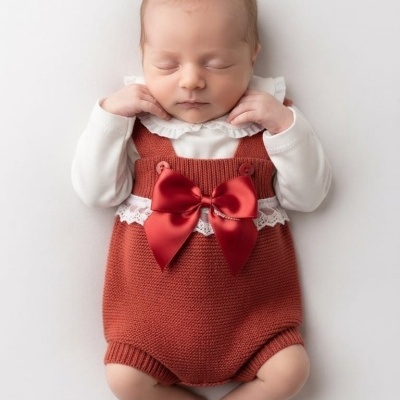 Bebé recém-nascido vestido com macacão vermelho com laço e body branco a dormir