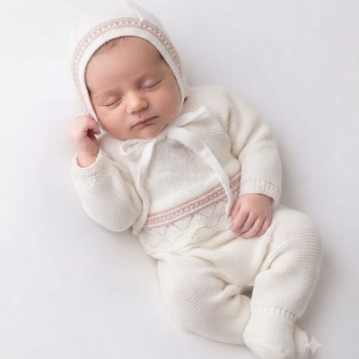 Bebé vestido com fato de malha branco com detalhes bege claro deitado