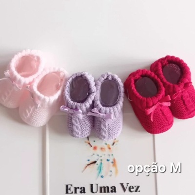 Sapatinhos de bebé em croché em três cores diferentes com cartão de apresentação da loja.