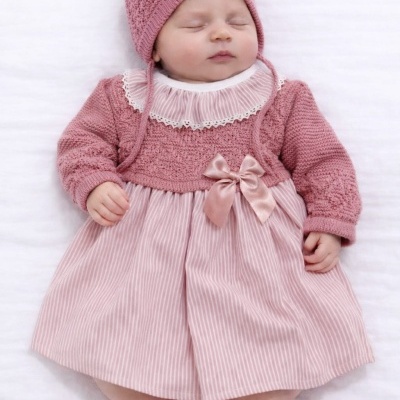 Bebé vestida com vestido rosa e gorro de malha, a dormir sobre fundo branco