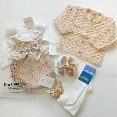 Conjunto de roupa de bebé beige e branco com vestido, casaco, sapatos e meias em fundo branco