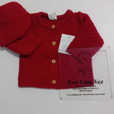 Casaco vermelho de bebé com botões de madeira e gorro vermelho sobre fundo branco.