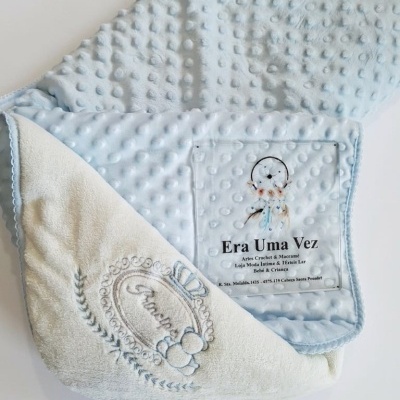 Manta infantil azul clara com pontos em relevo e verso felpudo branco bordado.