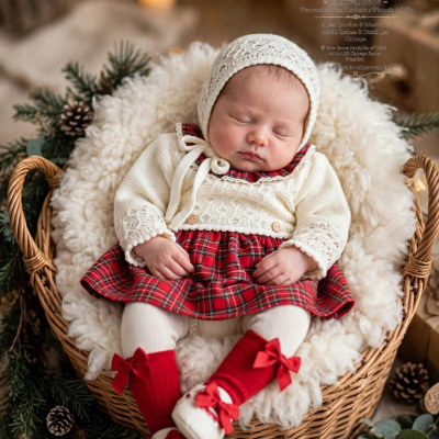 Bebé adormecido com roupa de xadrez vermelho e branco e casaco creme num ambiente acolhedor e com decoração natalícia