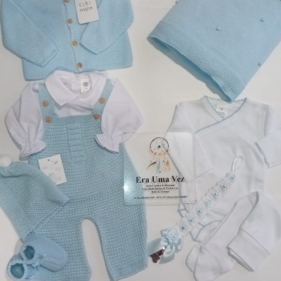 Conjunto de roupa de bebé azul e branco com malha, casaco, touca, sapatinhos, manta e prendebiberão.