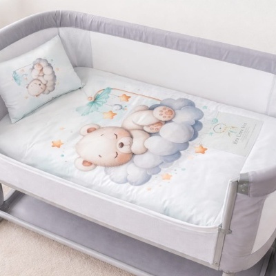 Berço cinza claro com colchão e almofada decorados com ursinho e carneirinho em ambiente claro
