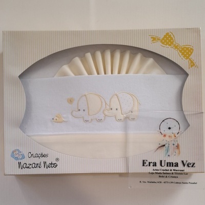 Caixa bege com riscas brancas contendo têxtil branco bordado com elefantes, com texto na embalagem