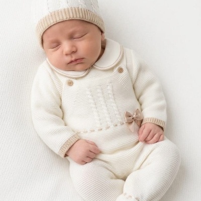 Bebé recém-nascido a dormir com roupa de malha branca e bege e gorro branco e bege