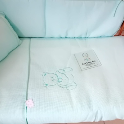 Berço com roupa de cama azul clara e ursinho bordado