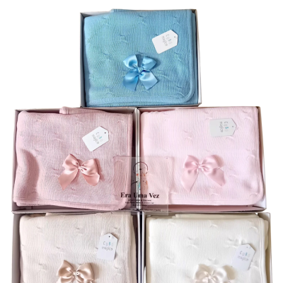 Mantinhas de bebé em várias cores com laços e etiquetas em caixas.