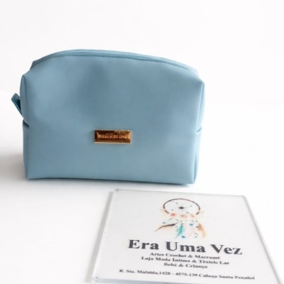 Bolsa pequena azul clara com placa dourada e cartão com texto e ilustração