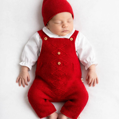 Bebé com macacão vermelho de malha e gorro vermelho com pompom
