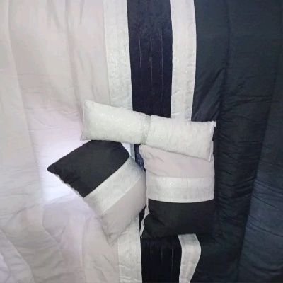 Colcha e almofadas preto, branco e cinza com padrão de faixas texturizadas, em espaço interior.