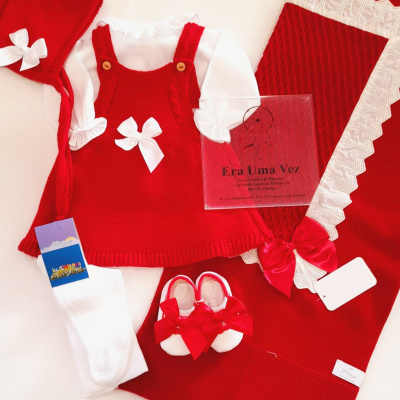 Conjunto de roupa de bebé vermelho e branco com saia, body, touca, meias, sapatinhos e manta com laços e bordado.