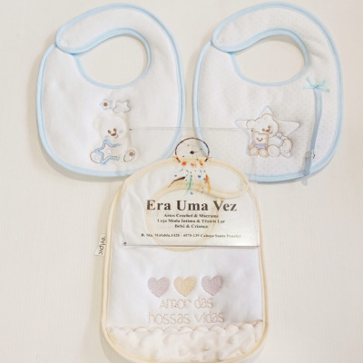 Três babetes de bebê branco com bordas azuis e bege, detalhes bordados de ursinhos e corações, sobre fundo branco liso.