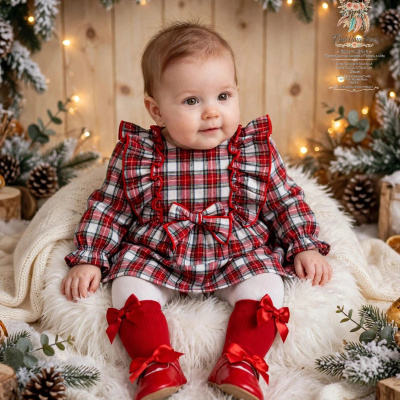 Bebé com vestido xadrez vermelho e branco e botins vermelhos num cenário natalício