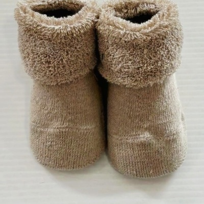 Botas de bebé castanhas felpudas com parte superior dobrada sobre superfície branca