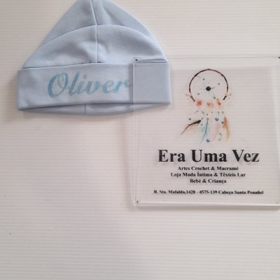 Gorro azul claro para bebé com nome bordado e cartão de empresa ao lado