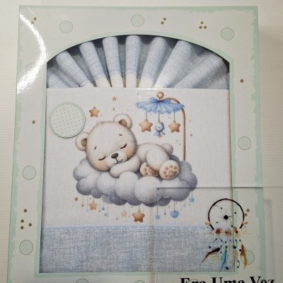 Jogo de cama para bebé azul com urso a dormir numa nuvem e estrelas, embalagem branca com bolinhas verdes.