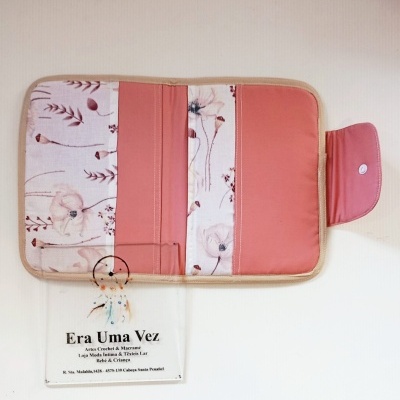Carteira de tecido rosa e bege com padrão floral e fecho de pressão numa superfície branca com cartão de visita