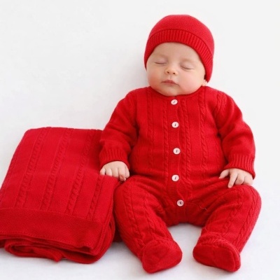 Bebé vestido com macacão vermelho de malha e gorro com uma manta vermelha ao lado