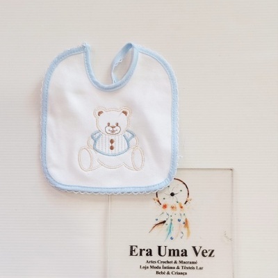 Babete branco e azul com ursinho bordado e cartão de loja em fundo branco