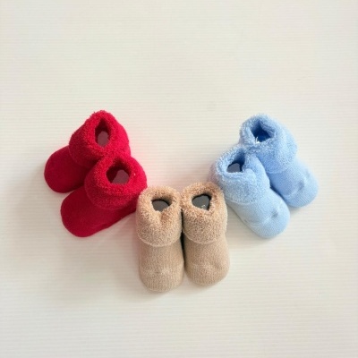 Três pares de meias-botas felpudas para bebés em vermelho, bege e azul claro sobre fundo branco
