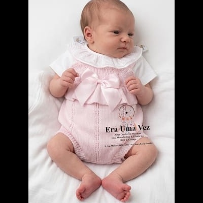 Bebé com roupa rosa de malha e body branco deitado em fundo branco