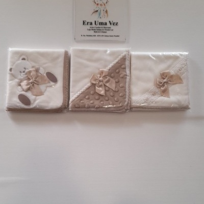 Três mantas para bebé em tons bege e branco com laços e urso bordado