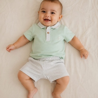 Bebé sorridente deitado com roupa verde clara e calções listrados cinza e branco