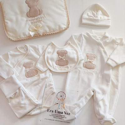 Conjunto de roupa de bebé branca com ursinho bordado e manta acolchoada.