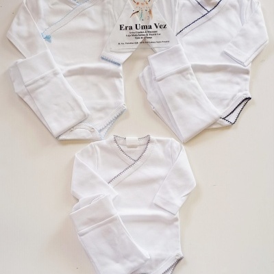 Três conjuntos de roupa de bebé branca com detalhes coloridos e cartão de loja em fundo branco