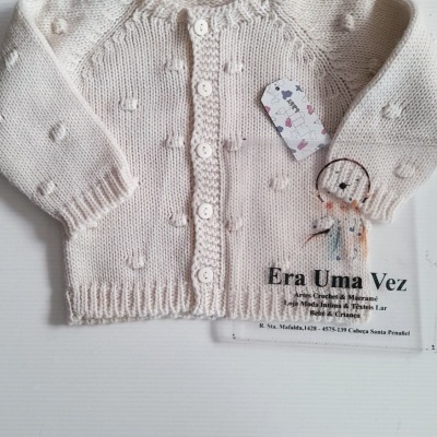 Camisola de bebé branca com botões e textura em bolinhas, etiqueta pendurada e cartão com texto