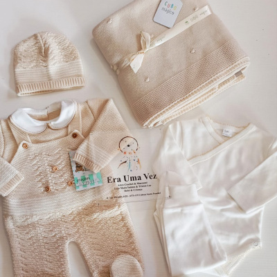 Conjunto de bebé com body branco, macacão bege, gorro, sapatinhos e manta dobrada
