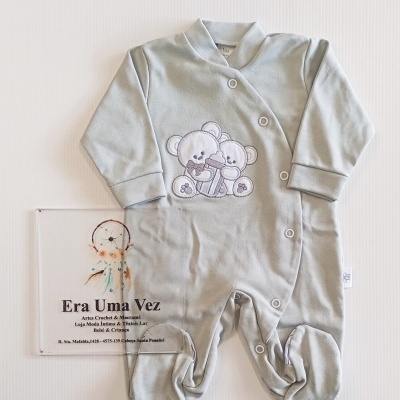 Pijama verde claro de bebé com ursinho bordado e botões, colocado sobre fundo branco com placa era uma vez