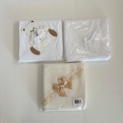 Três mantas de bebé embaladas, duas brancas e uma bege com laços e bordados.