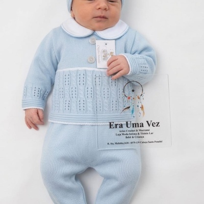 Bebé com conjunto azul claro de malha e gorro segurando etiqueta, placa transparente com texto ao lado