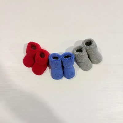 Três pares de meias antiderrapantes para bebé em vermelho, azul e cinzento sobre superfície branca