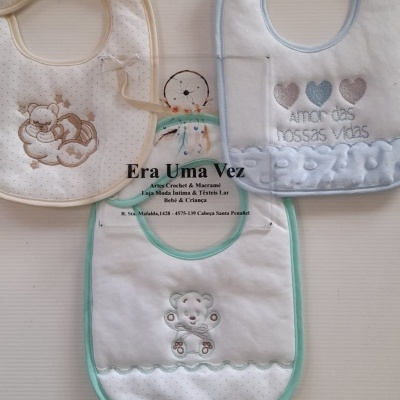 Três babetes de bebé em tecido branco com bordados e detalhes em bege, verde e azul