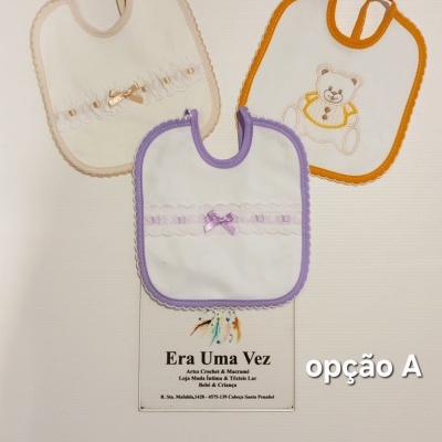 Três babetes de bebé brancos com bordas coloridas e detalhes delicados em fundo branco