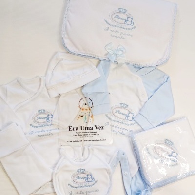 Conjunto de roupa de bebé branco e azul claro com bordados e fita azul.