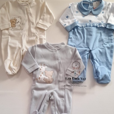 Três macacões de bebé em tecidos branco, azul e cinza com bordados e padrões de ursinhos e girafas.
