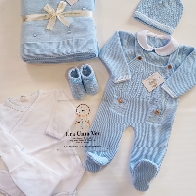 Conjunto de bebé azul claro em malha com body branco e acessórios em fundo claro.
