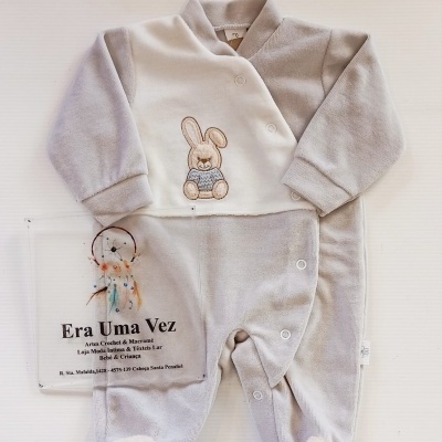 Pijama cinzento e creme para bebé com coelho bordado e botão, junto a cartaz promocional Era Uma Vez.