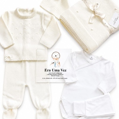 Conjunto de roupa de bebé branco com fatos de malha, gorro, manta e body, etiqueta NOVOMARÃO e cartão Era Uma Vez.