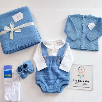 Conjunto de roupa de bebé azul com camisola, body, jardineira, sapatinhos, meias e manta com etiquetas.