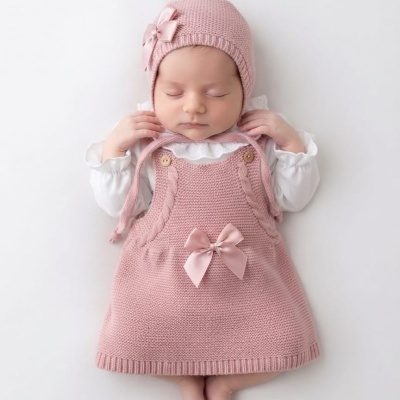 Bebé com vestido rosa de malha e gorro rosa com laço de fita