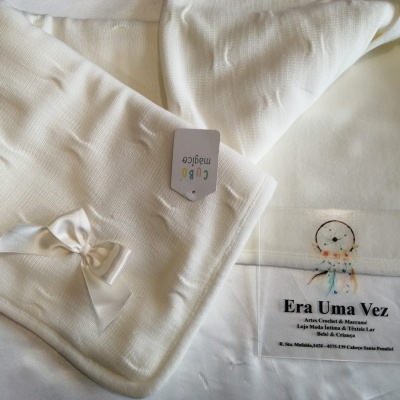 Manta branca para bebé com laço de fita e etiqueta CuBo Magico, junto a cartaz Era Uma Vez Artes