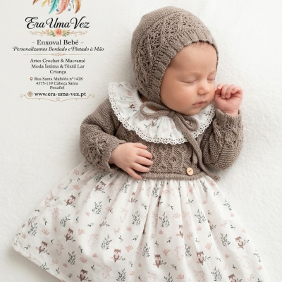 Bebé a dormir com traje de croché cinza e vestido branco com padrão de corujas